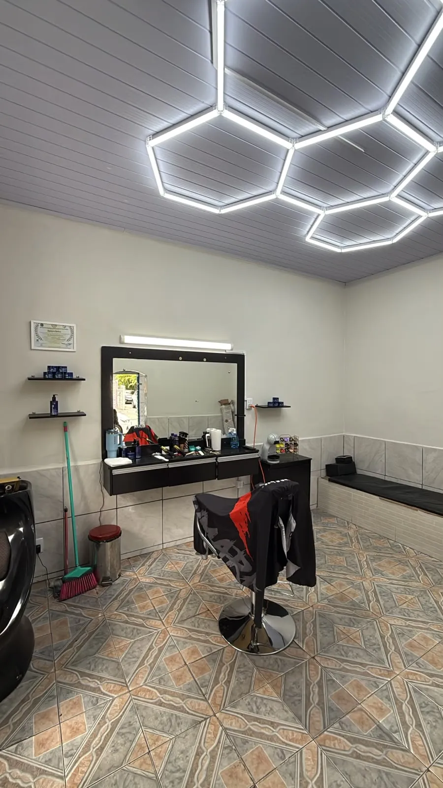 Interior da Macedo Barbearia, com a cadeira, o espelho e as luzes hexagonais no teto